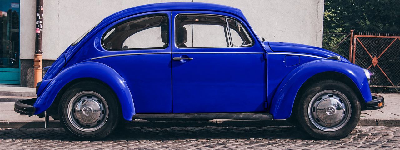 Blauer VW Käfer am Straßenrand auf Kopfsteinpflaster