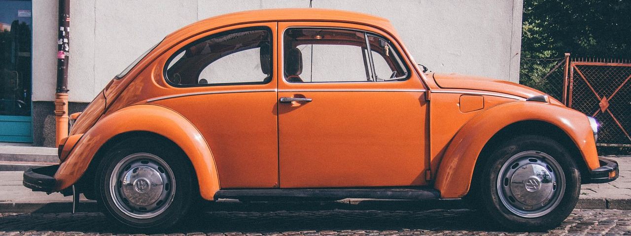 Orangefarbener VW Käfer am Straßenrand auf Kopfsteinpflaster